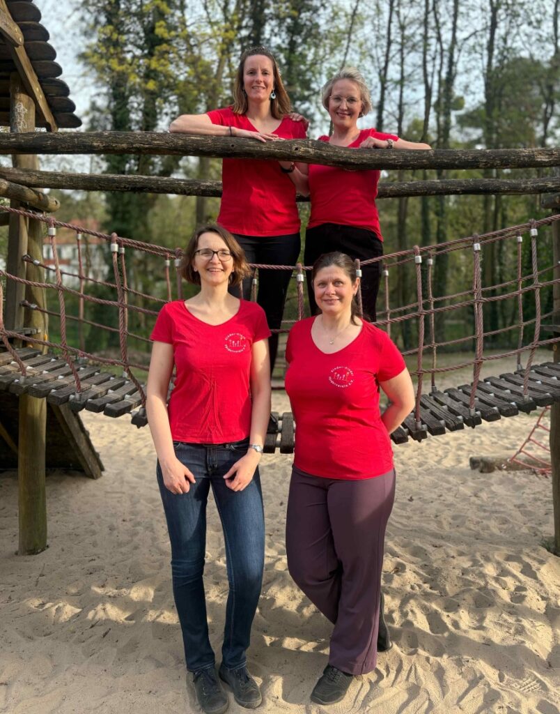 Vorstand_Kikive_2025_kleiner Vorstand Kinder-Kinder Förderverein e.V. vier Frauen mit roten T-Shirts vor der Hängebrücke eines Klettergerüsts